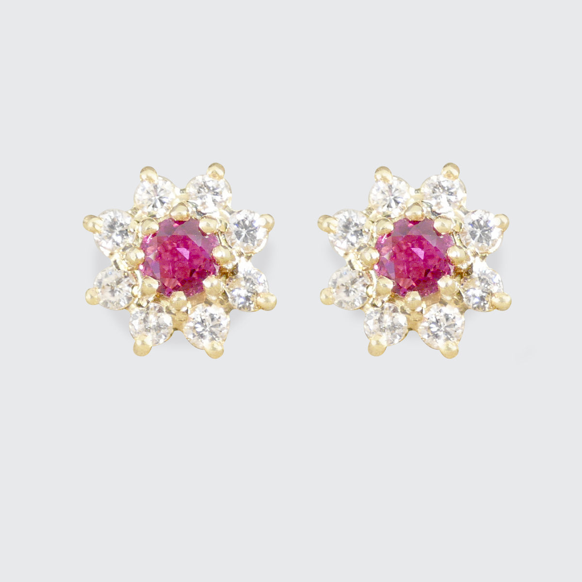 Pair of gold earrings with pink/red rubiy gemstones on a light gray background