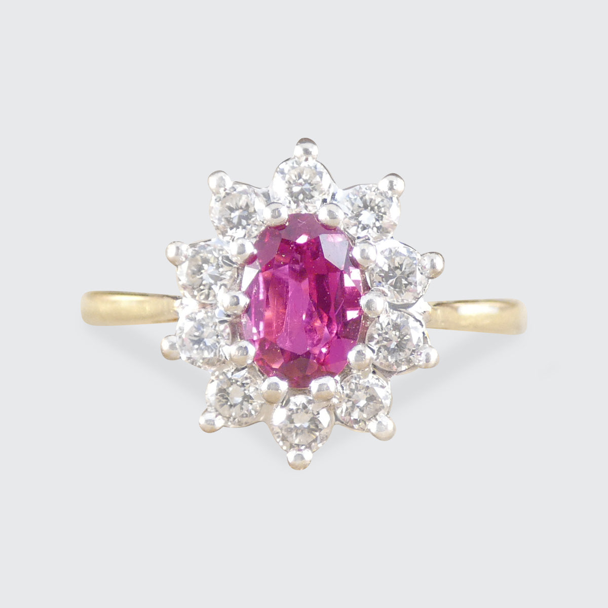 Ring with a pink ruby gemstone and diamond stones clustering on a light gray background