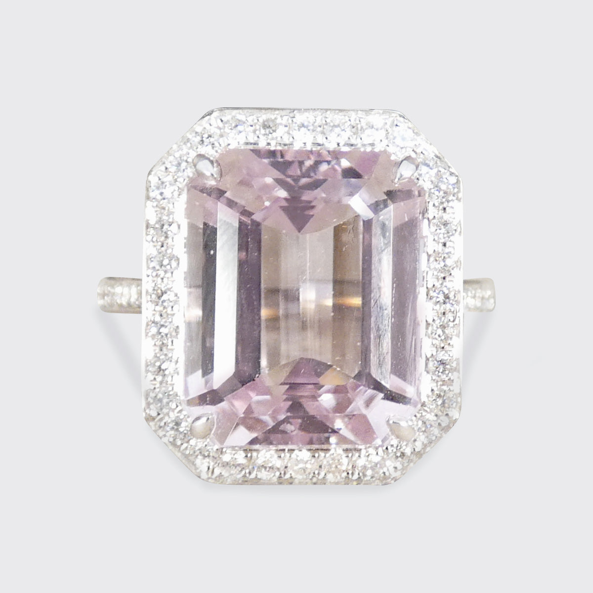 Pink gemstone ring with diamond halo on a light gray background