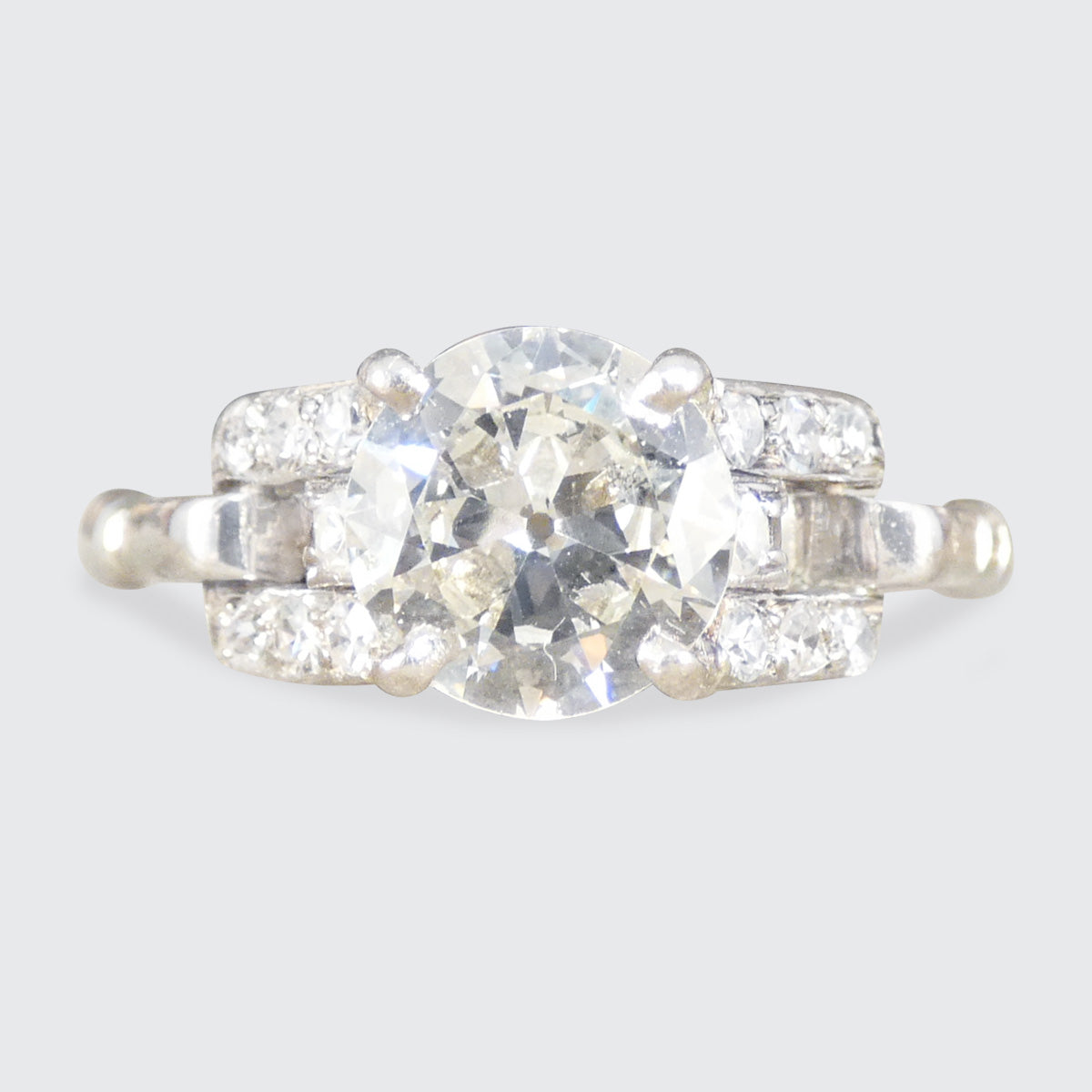 Diamond ring with a central stone and smaller stones on a light gray background