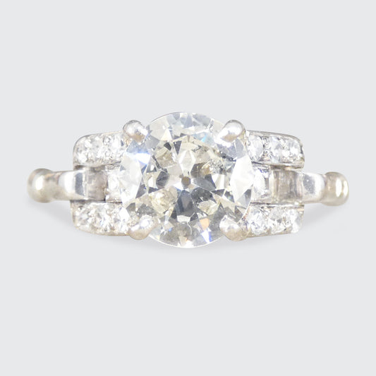 Diamond ring with a central stone and smaller stones on a light gray background