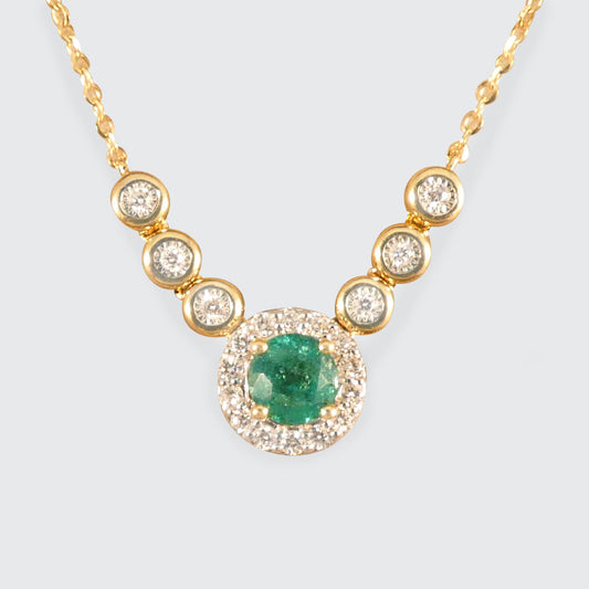 A stunning new necklace crafted in 18ct yellow gold, featuring a vibrant green emerald centre piece surrounded by a halo of sparkling diamonds, complemented by additional bezel-set diamonds in an illusion setting along the chain.