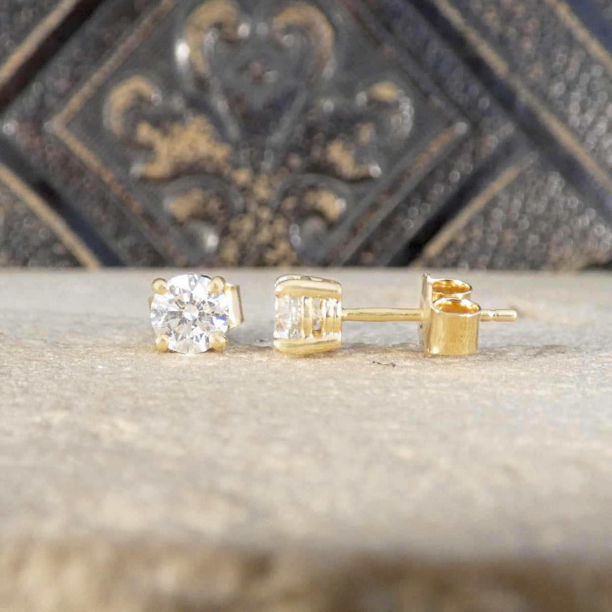 Gold diamond stud earrings on a textured surface with a decorative background