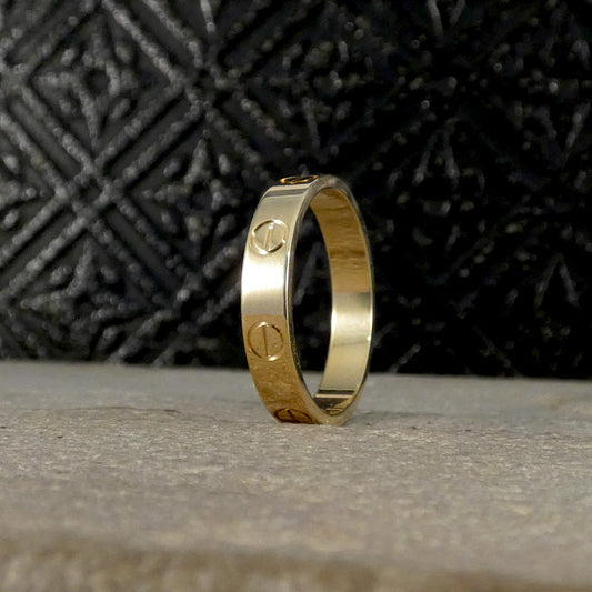 Close-up of a Cartier Love ring in 18ct yellow gold featuring iconic screw motifs, set against a textured dark background.