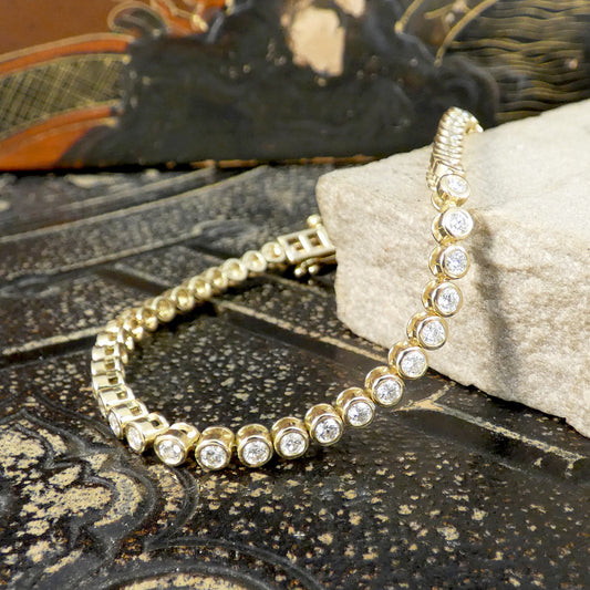 Gold tennis bracelet with diamond in full gold bezel rub over settings on a textured surface