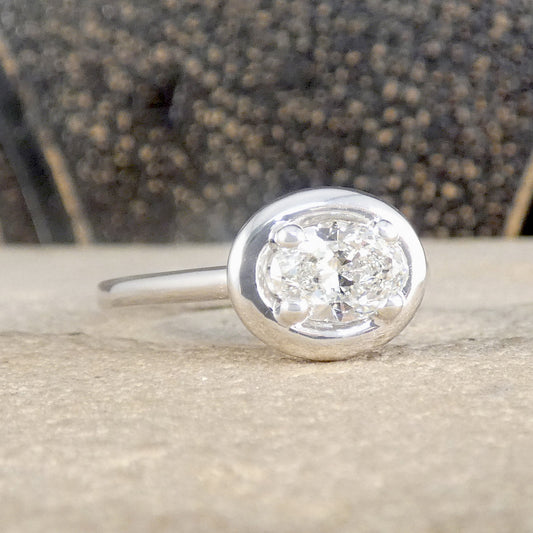 A platinum bezel-set diamond ring resting on a textured stone surface with a blurred dark background.