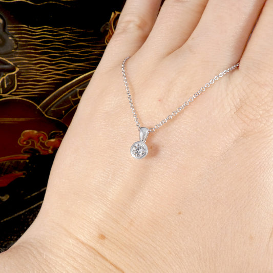 White gold necklace with a round pendant on a hand against a decorative background