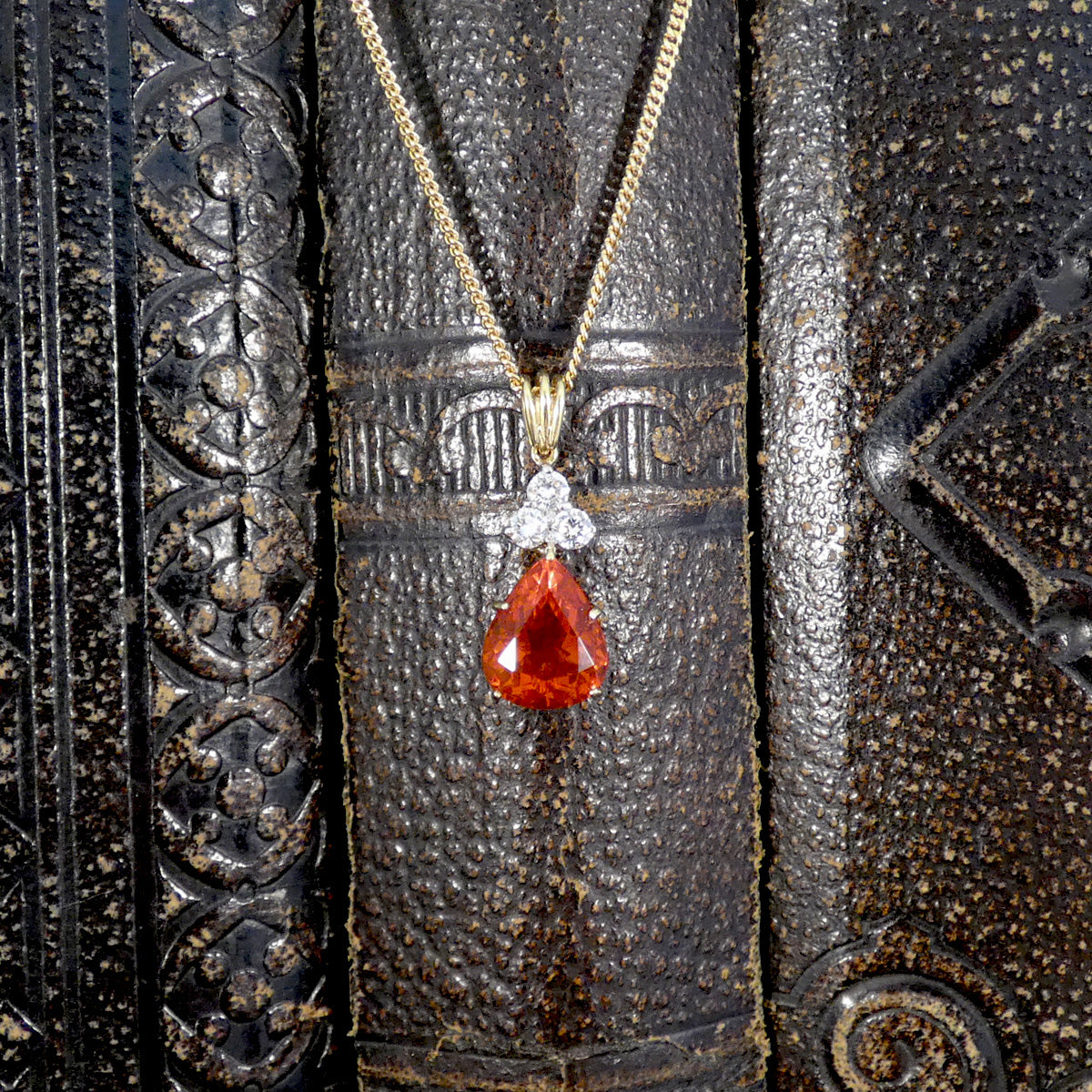 Red teardrop Fire Opal pendant with gold chain on textured black background