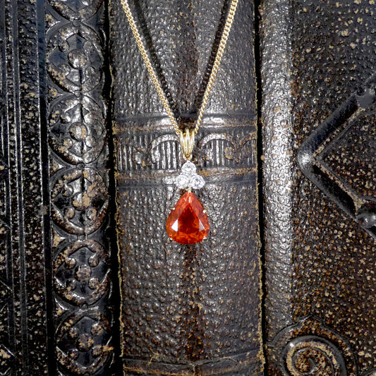 Red teardrop Fire Opal pendant with gold chain on textured black background