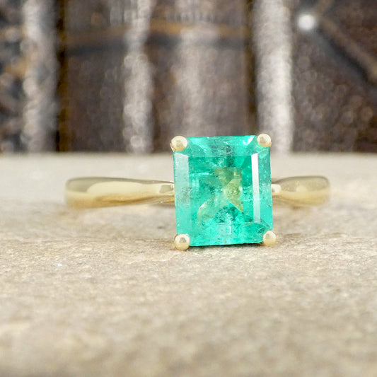 Gold ring with a green emerald stone on a textured surface
