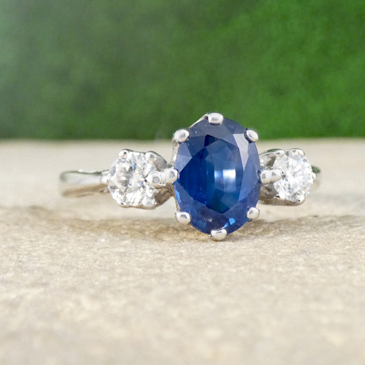 Ring with a blue gemstone and diamond accents on a textured surface with a green background