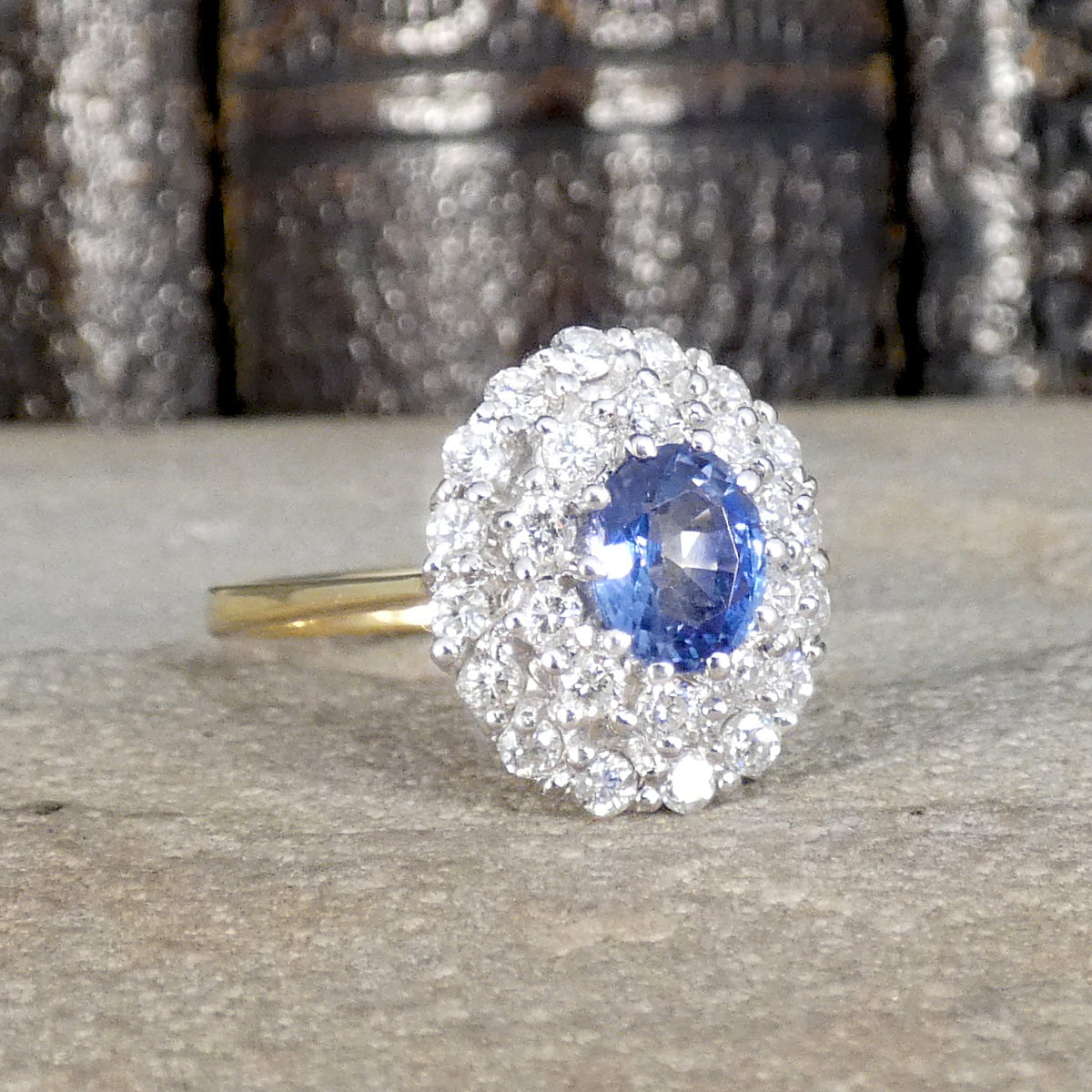 Vintage-style cluster ring featuring a central oval blue sapphire surrounded by multiple round brilliant-cut diamonds, set in white and yellow gold.
