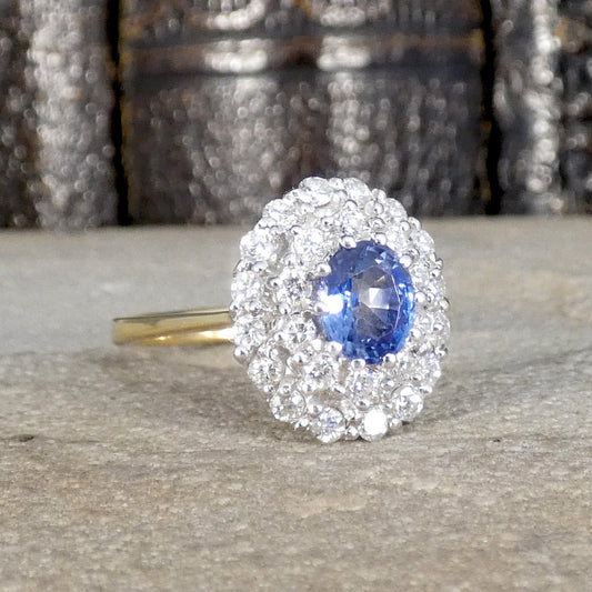 Vintage-style cluster ring featuring a central oval blue sapphire surrounded by multiple round brilliant-cut diamonds, set in white and yellow gold.