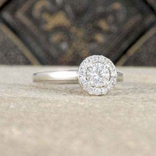 Diamond ring with a halo setting on a textured surface with a blurred decorative background