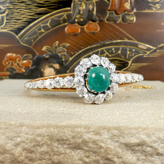 Late Victorian cabochon emerald and diamond bangle, showcasing a central emerald surrounded by a halo of old-cut diamonds, set in yellow gold with intricate details.