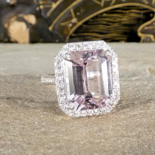 Ring with a pink gemstone and diamond-studded halo on a textured surface