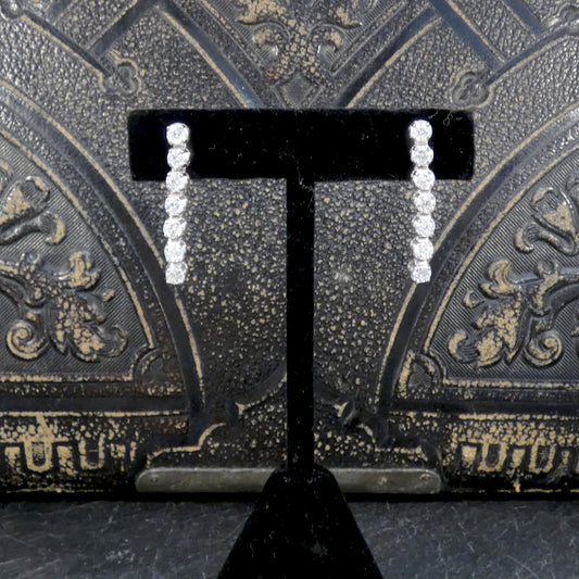 Pair of diamond drop earrings on a black earring stand against an ornate black background