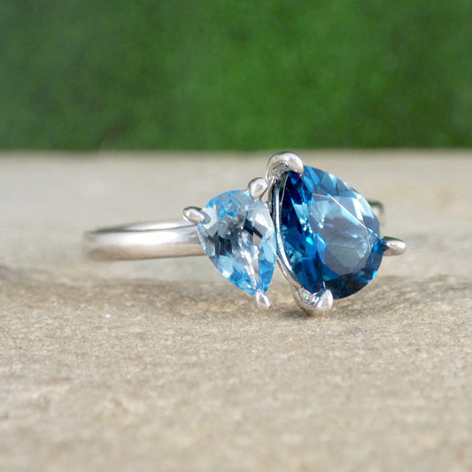 Silver ring with two blue pear-shaped gemstones on a textured surface with a green background