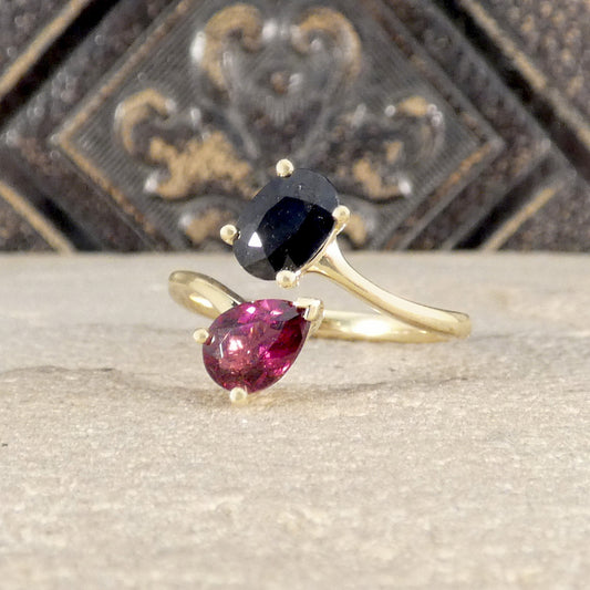 Gold ring with a black gemstone and a pink gemstone on a textured surface.