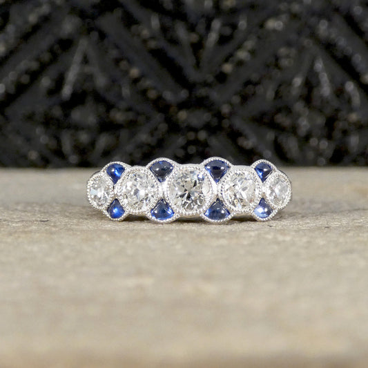 Art Deco-inspired diamond and sapphire ring in platinum, featuring five old-cut diamonds accented by vivid blue triangle-cut sapphires in a milgrain setting, creating a vintage eternity band style.