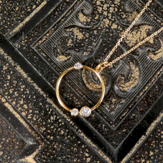 Gold necklace with a circular pendant featuring three diamonds on an ornate black background.