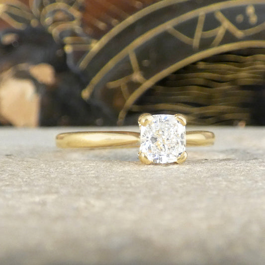 18-carat yellow gold solitaire ring featuring a GIA-certified modified cushion-cut diamond of E colour, displayed on a textured surface. The sleek band and radiant diamond combine for a timeless and elegant engagement ring design.