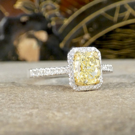 Diamond ring with a yellow cushion cut diamond and a halo of white diamonds on a textured surface