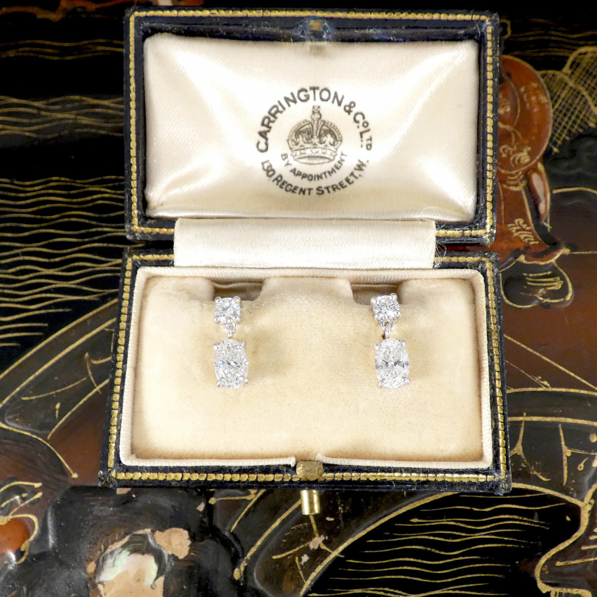 Diamond earrings in a Carrington & Co box on an ornate background