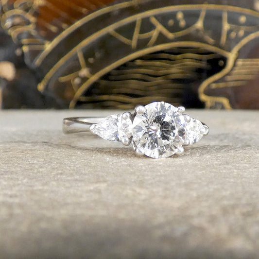 Diamond ring with pear-shaped side stones on a stone surface with a decorative object in the background