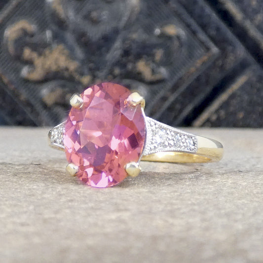 Sitting in a four claw gold setting is a vibrant pink tourmaline with diamond set shoulders graduating down in size down the shoulders leading to a plain polished 18ct yellow gold band.