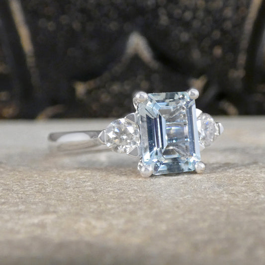 Modern Emerald Cut Aquamarine and 0.35ct Diamond Three Stone Ring in Platinum. The Diamonds are set in a triangle setting giving the illusion of trillion cut diamonds.
