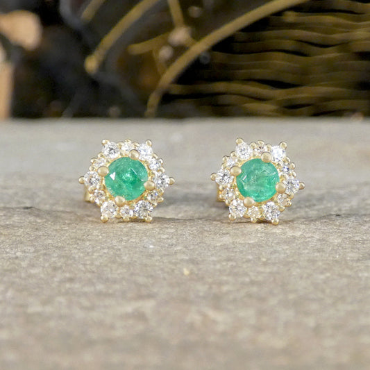 Pair of emerald and diamond stud earrings on a neutral background