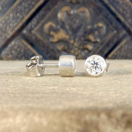 A classic pair of Bezel set Diamond Stud Earrings in Platinum holding 0.80ct with a GIA cert and bright E Colour grading. Showing one stud sat forward and the other to one side seeing the substantial butterfly back.