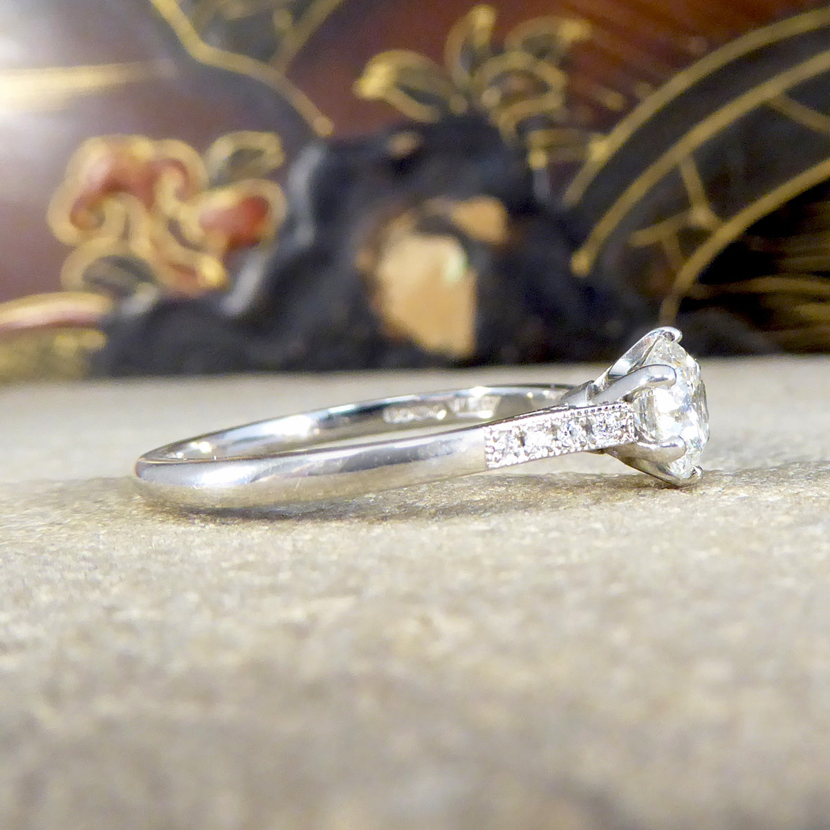 Side view of diamond ring with diamond set shoulder leading to a plain polished platinum band.