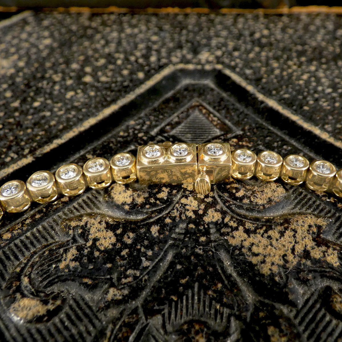 Gold bracelet with diamonds on a textured black background showing the snap lock clasp.