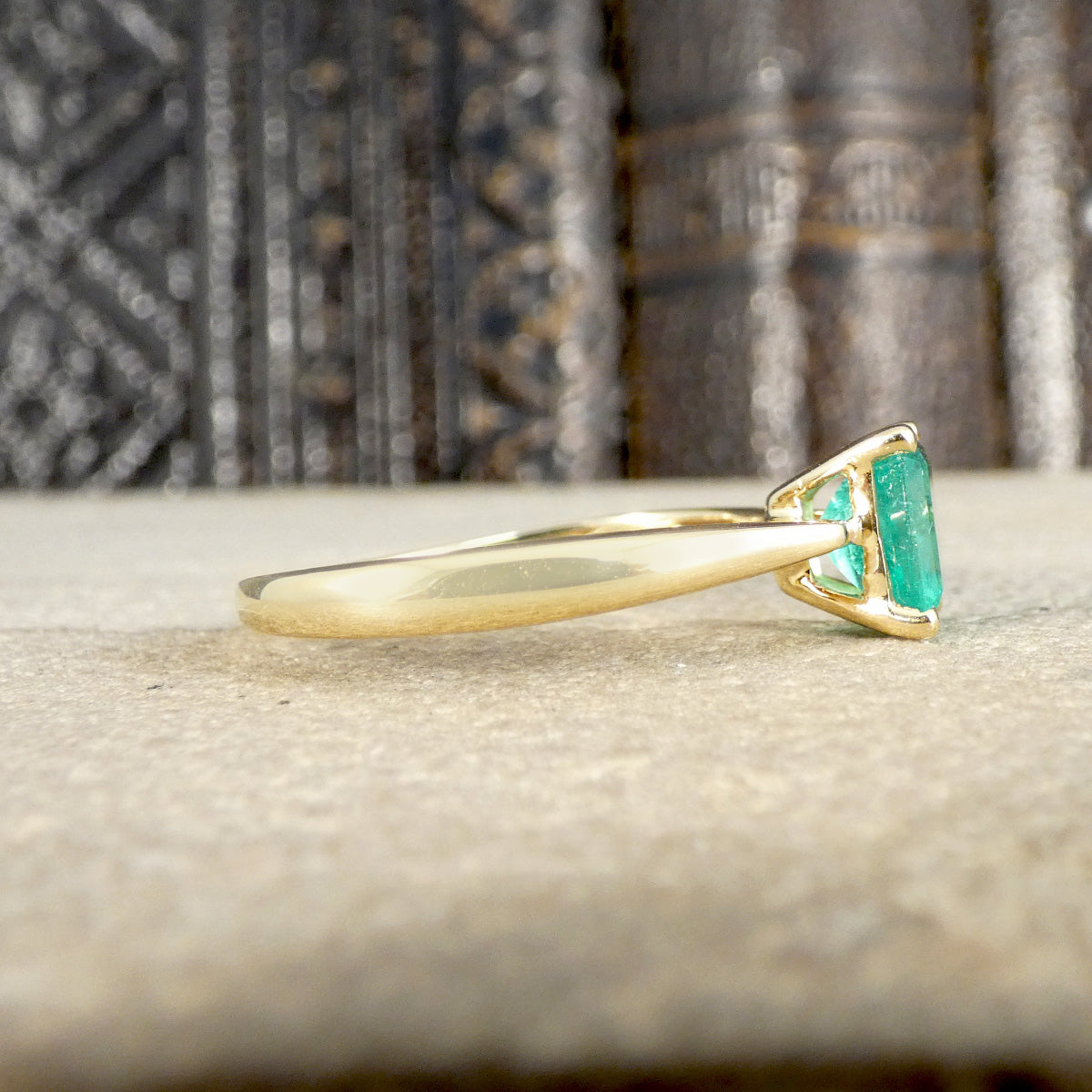 Gold ring with green gemstone on a textured surface shown from the side with plain polished band.