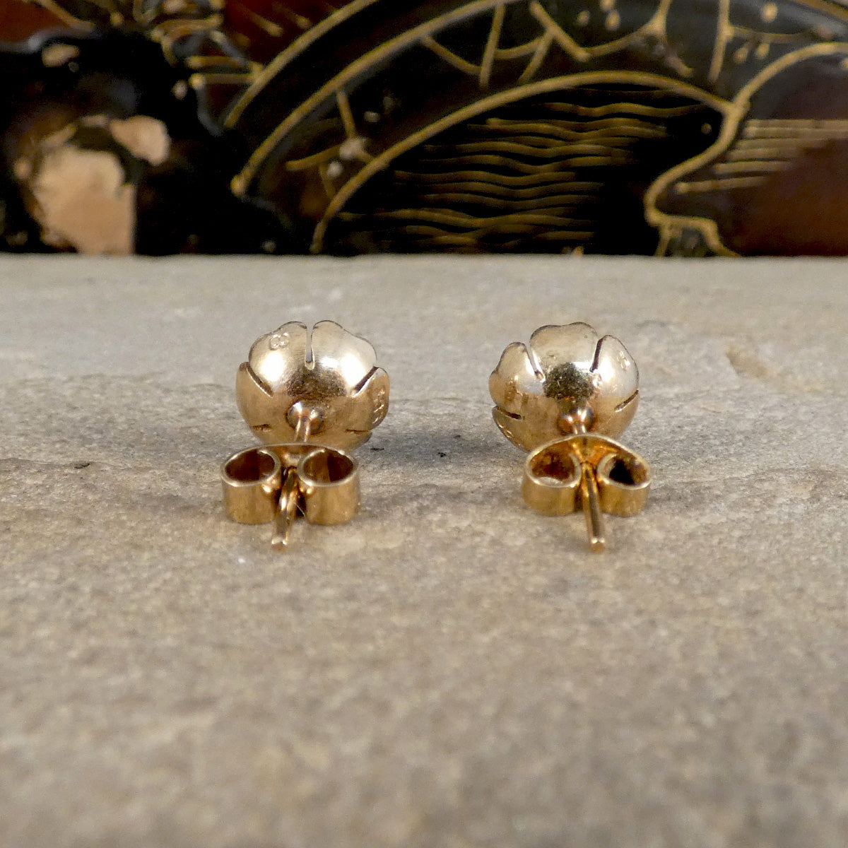 Gold flower-shaped earrings on a textured surface with a decorative background