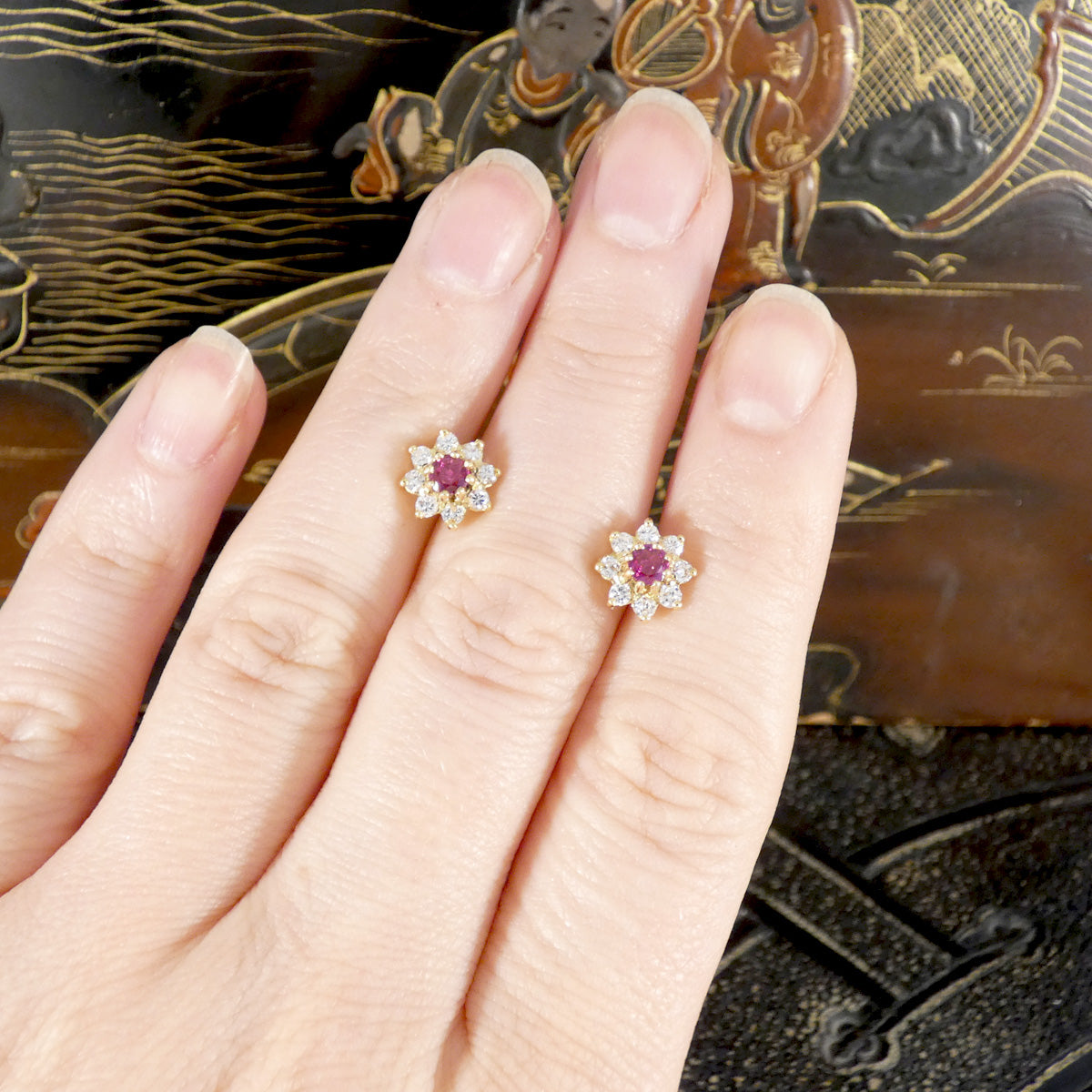 Gold and diamond earrings with gemstones on a hand against an ornate background