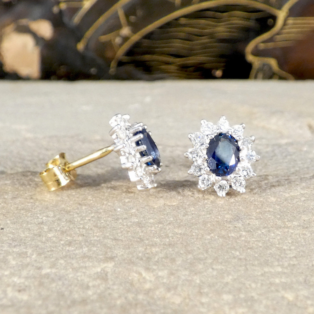 Pair of blue sapphire gemstone earrings with gold and silver accents on a textured surface.