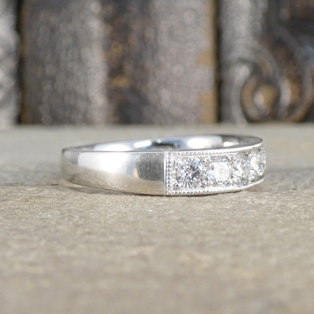 Platinum ring with diamond accents spreading half way around the ring on a textured surface