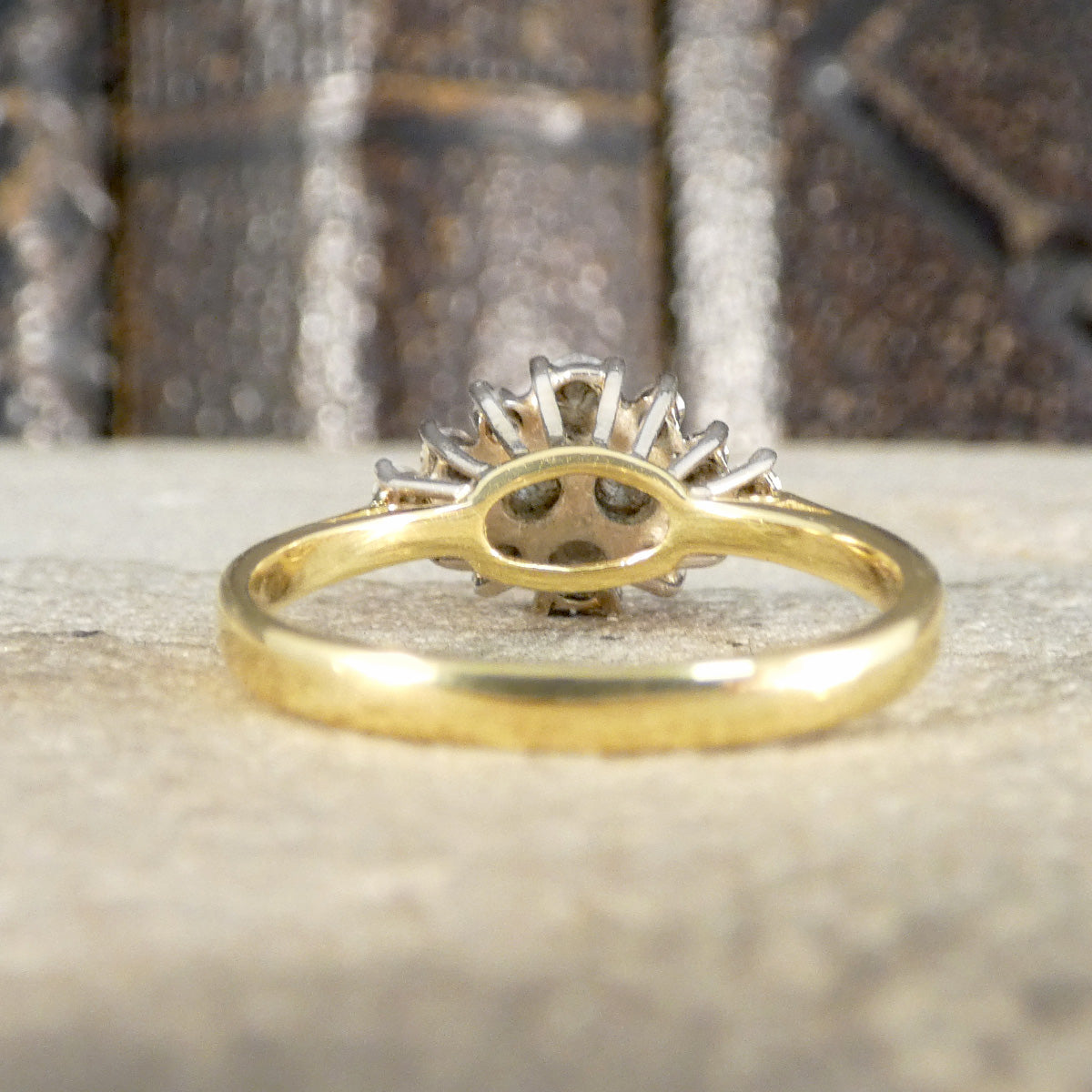 Gold ring with a diamond design on a textured surface shown from behind.