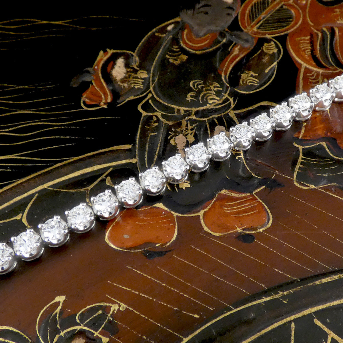 Close-up of a luxury diamond tennis bracelet in white gold, featuring round brilliant-cut diamonds in classic claw settings, displayed on an ornate lacquered background for an elegant and timeless aesthetic.