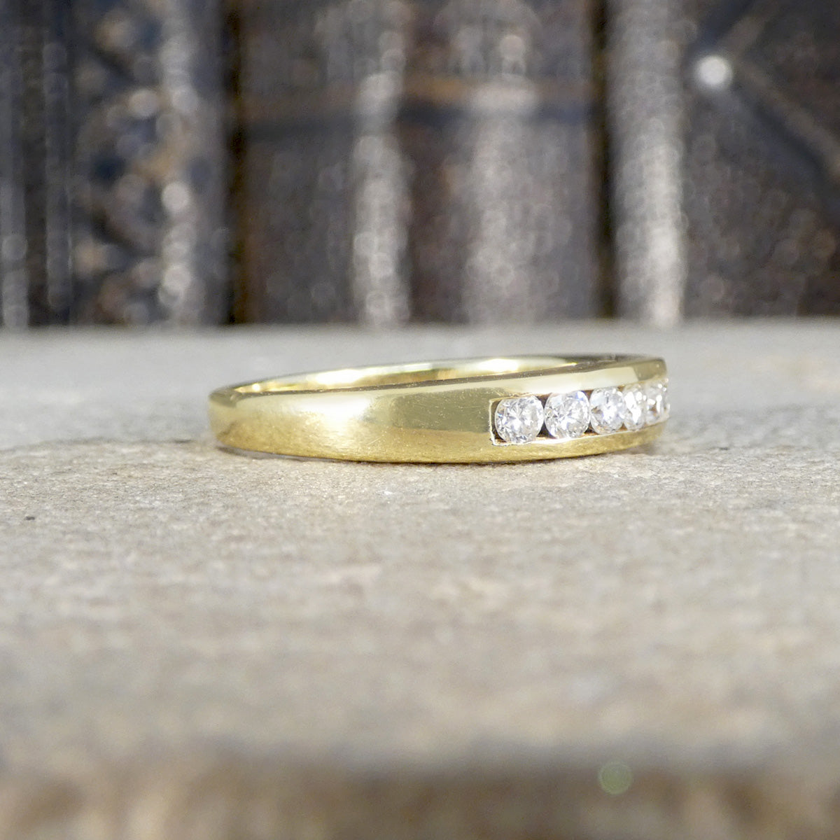 Gold ring with diamonds on a textured surface from the side showing how far diamonds are set.