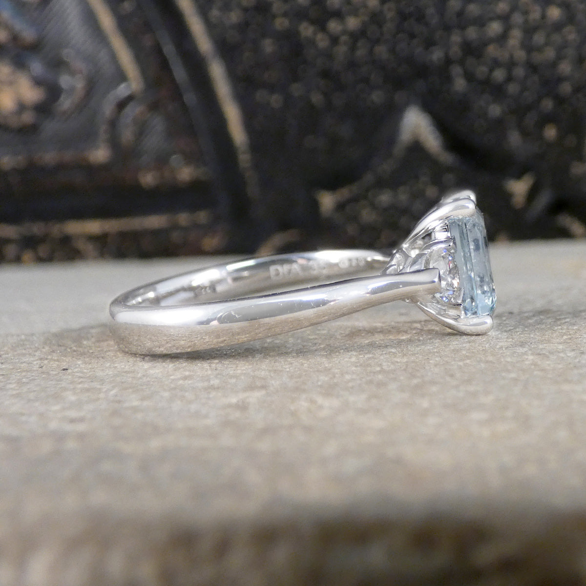 Side view of Modern Emerald Cut Aquamarine and 0.35ct Diamond Three Stone Ring in Platinum. Slightly tapered shoulders leading to. plain polished band and slight wedfit design for a perfect engagement ring.