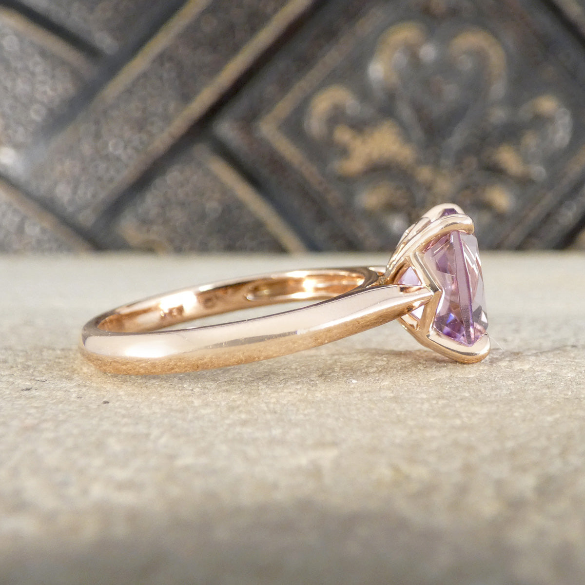Rose gold ring with a purple gemstone on a textured surface