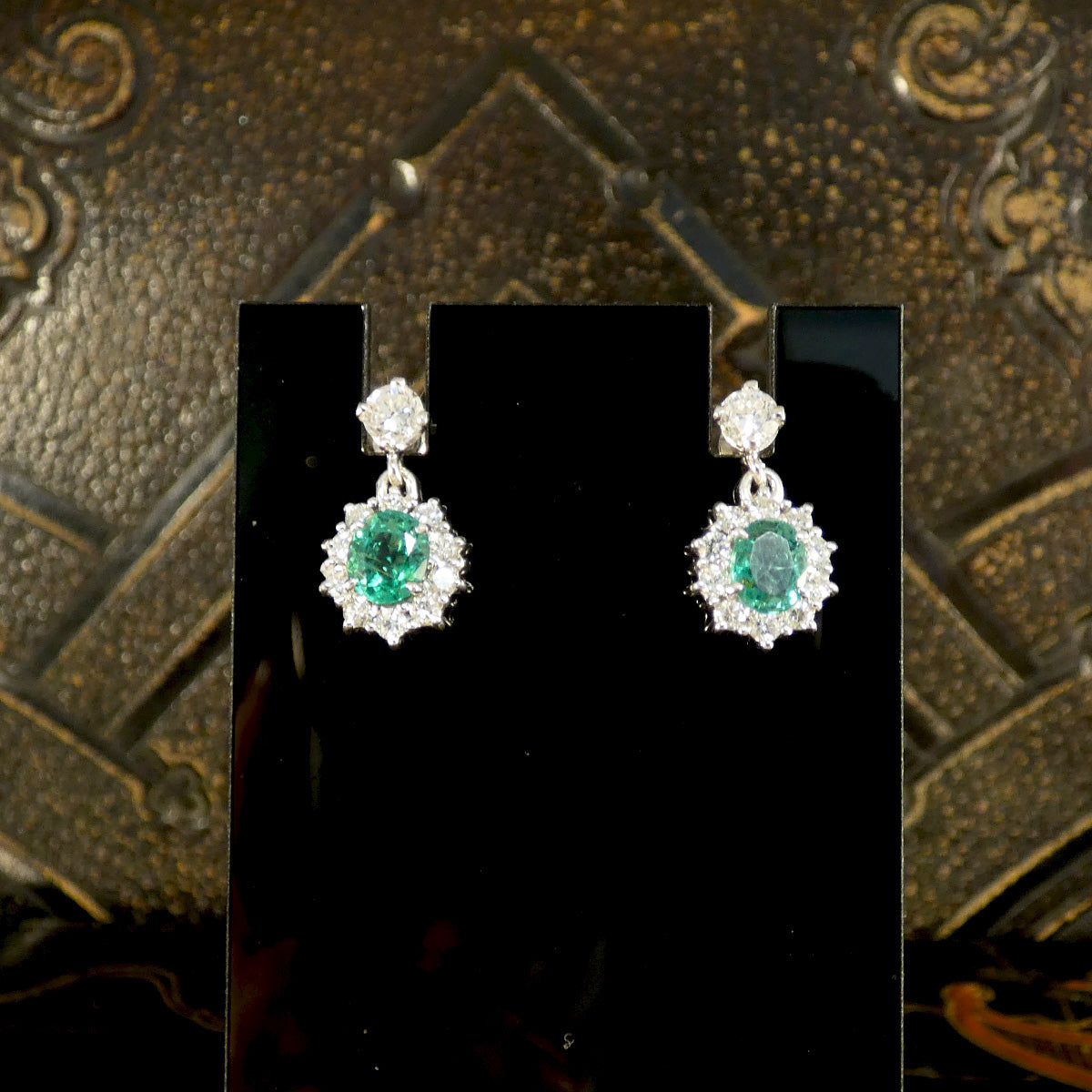 A beautiful pair of Oval Cut Emeralds surrounded by a halo of bright and sparkly diamonds hanging from a diamond stud as a drop earrings. Fully crafted in 18ct White gold, making the perfect gift.