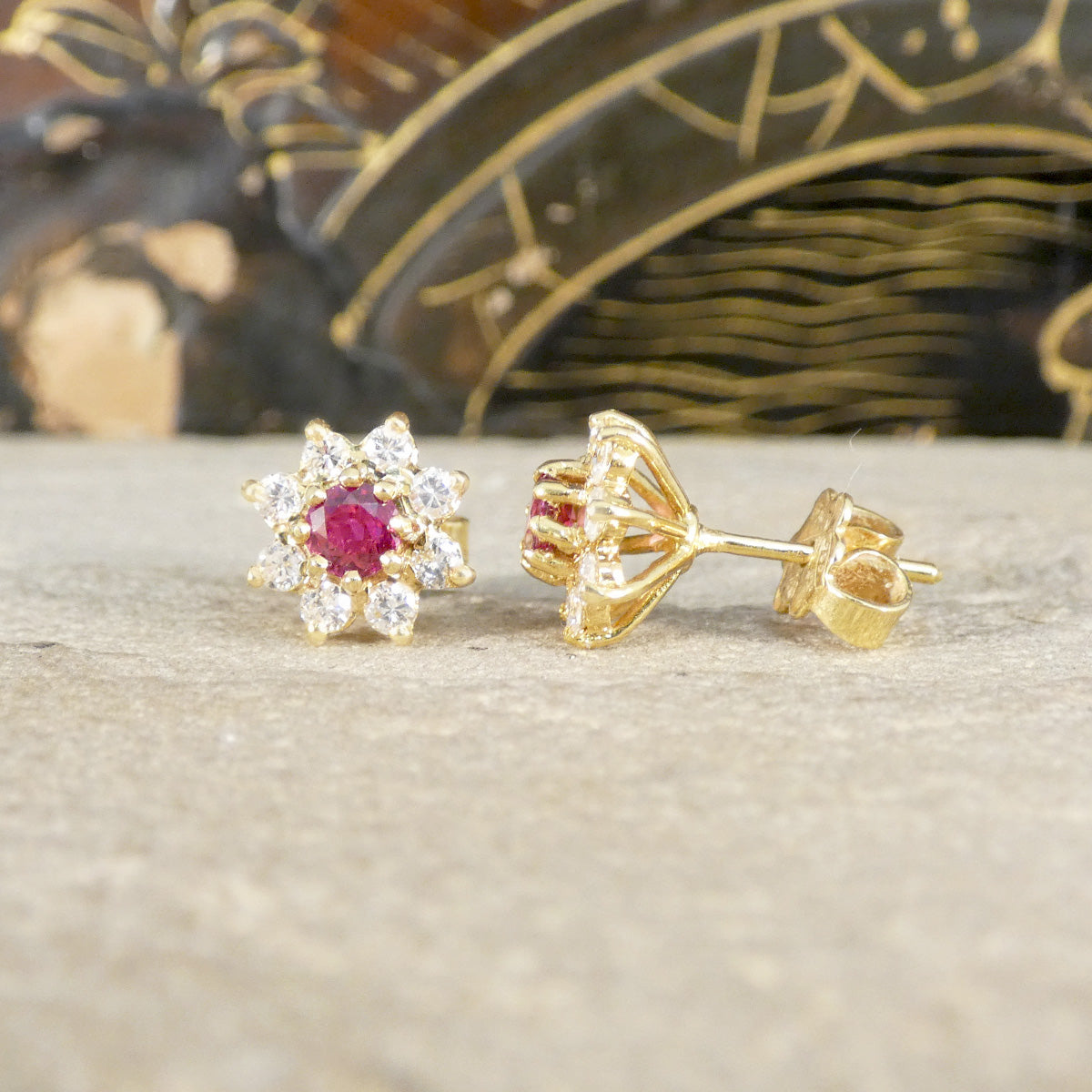 Gold earrings with red gemstones on a neutral background