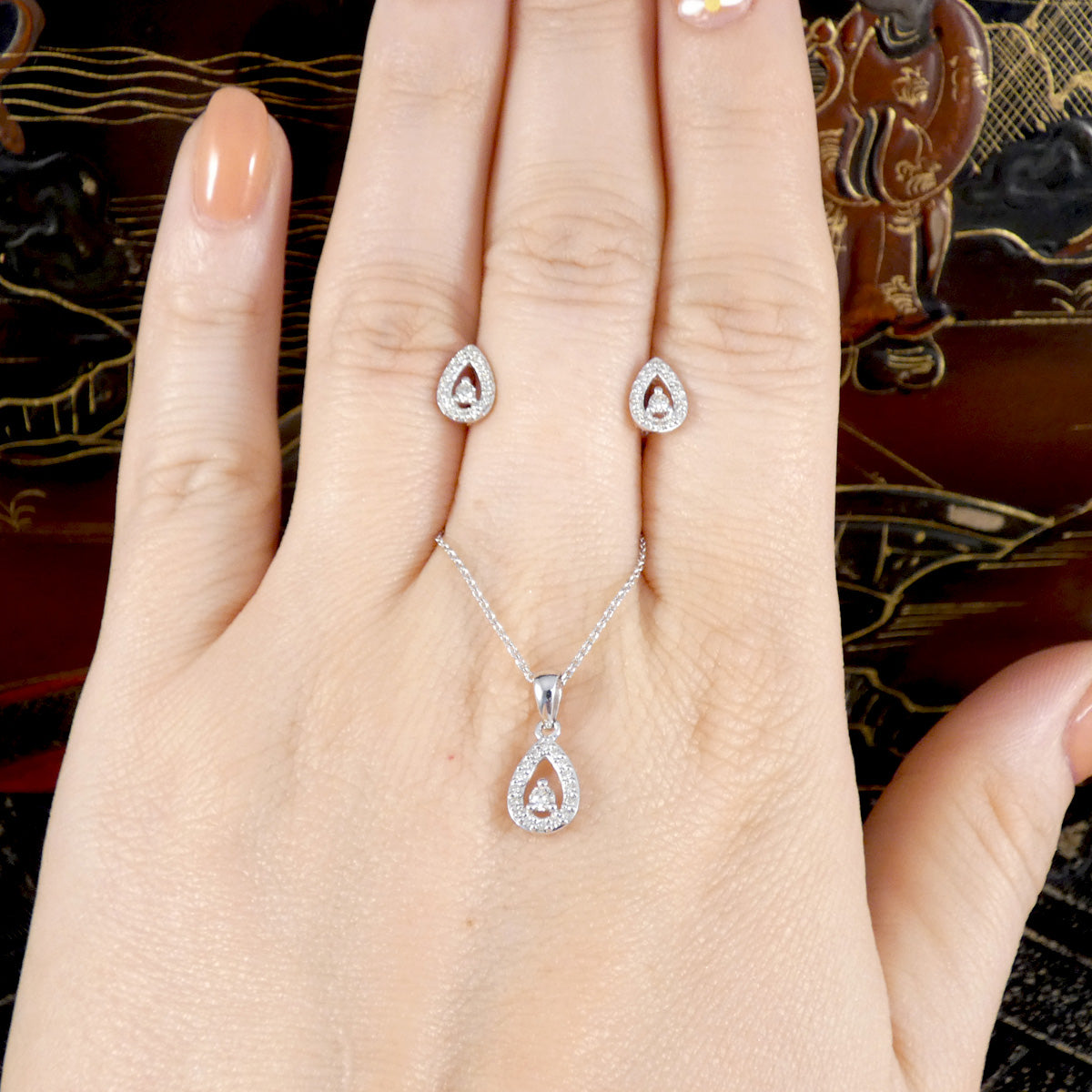 white gold jewellery set including necklace and earrings on a hand against a decorative background