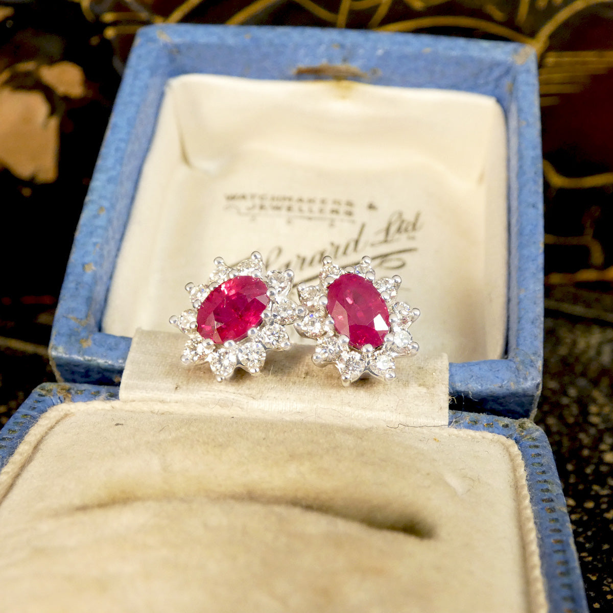 Ruby and Diamond Cluster Stud Earrings in 18ct White Gold, in a classic setting that will stand the test of time. Featuring a bright and pinkish oval cut Ruby in each stud with a cluster of Diamonds in 18ct White Gold. Displayed in vintage box, the perfect gift.