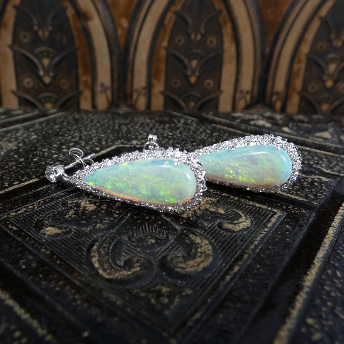 Side view of vintage opal and diamond cluster drop earrings in platinum, showcasing the vivid play-of-colour in the pear-shaped opals surrounded by a halo of sparkling diamonds.